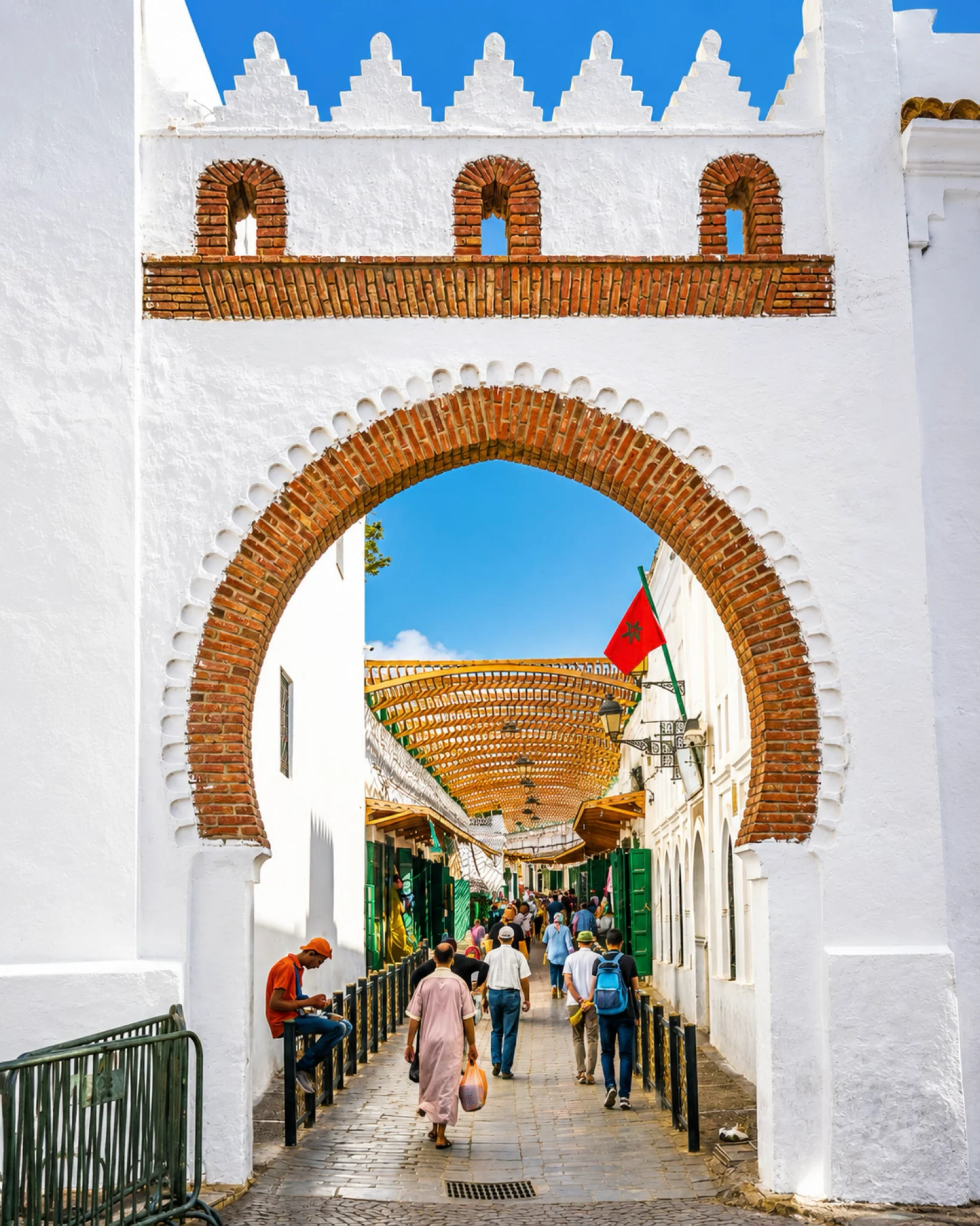 People entering a market street through a white brick arch in Tétouan